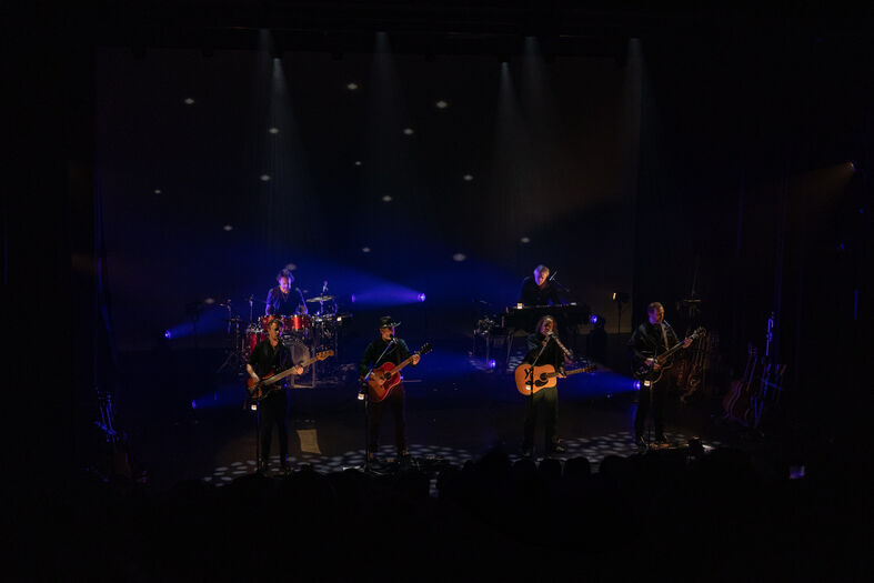 Een band speelt live op een podium, omringd door sfeervolle verlichting en een duistere achtergrond.