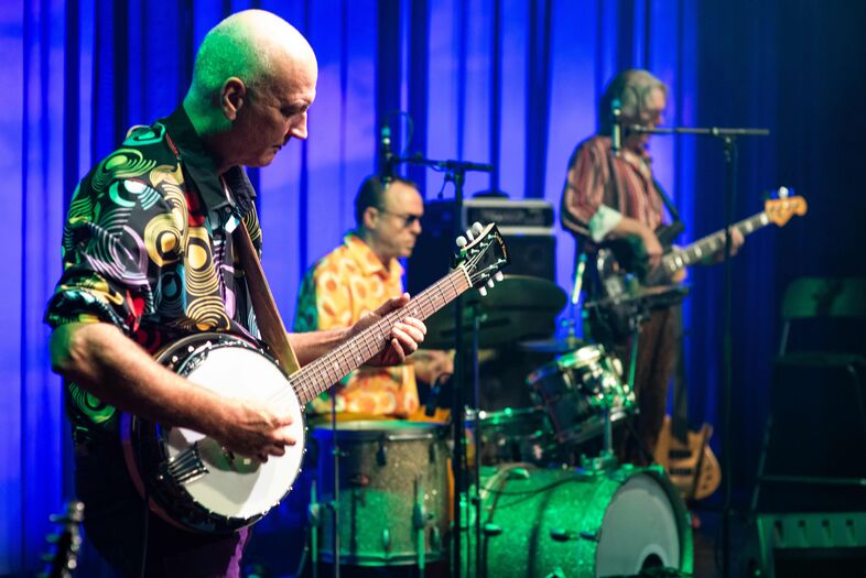 Drie muzikanten op een podium, spelen verschillende instrumenten in een kleurrijke, sfeervolle setting.