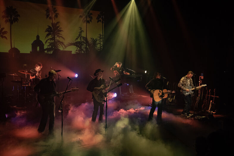 Muzikanten op het podium, omringd door rook en lichteffecten tijdens een live optreden.