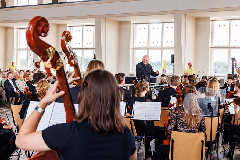 Een orchestrapport met muzikanten die optreden, gezien vanaf de achterkant van een contrabas.