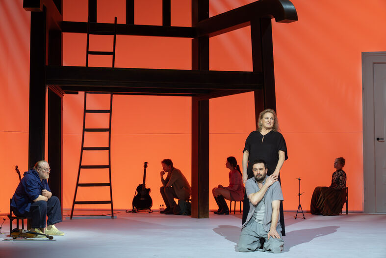 Ensemble op toneel rond oversized stoel en ladder in warme verlichting.