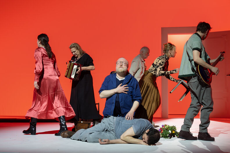 Groep performers beweegt rond persoon op vloer terwijl anderen instrumenten bespelen.