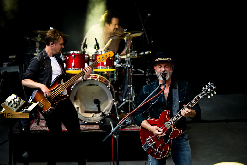 Muzikanten spelen live op een podium, met een gitarist, bassist en drummer in actie.