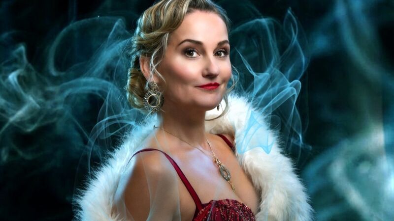 Een vrouw in glamour kleding met een witte bontjas, poseert met een elegante uitstraling en een vage rookachtergrond.