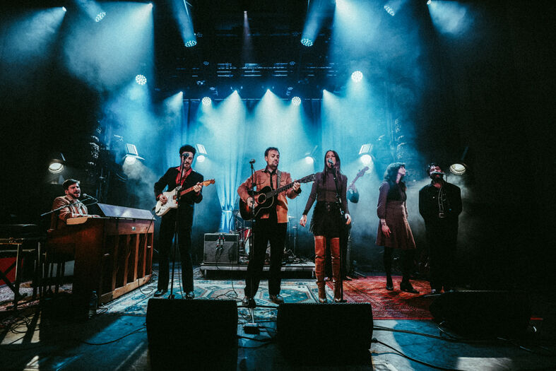 Muzikanten spelen op donker podium met felblauwe lichten en instrumenten.