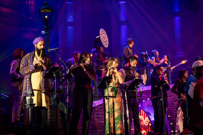 Een divers ensemble van muzikanten speelt verschillende instrumenten op een kleurrijk verlichte scène.