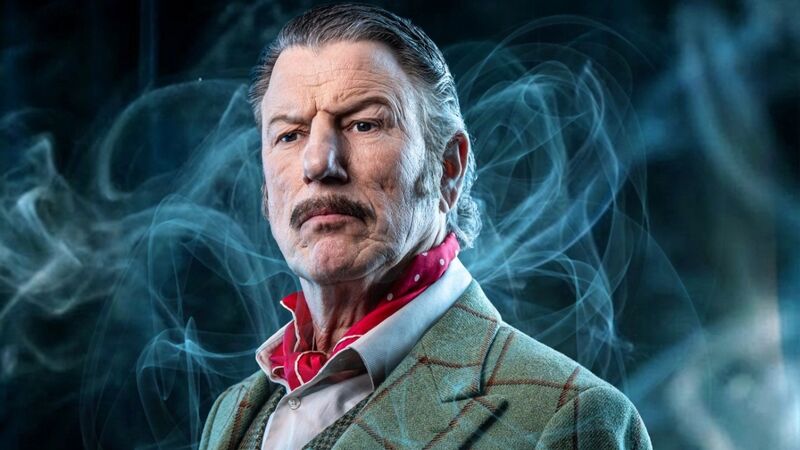 Portret van een man met een snor, gekleed in een lichte jas en een rode sjaal, omgeven door een dampige sfeer.