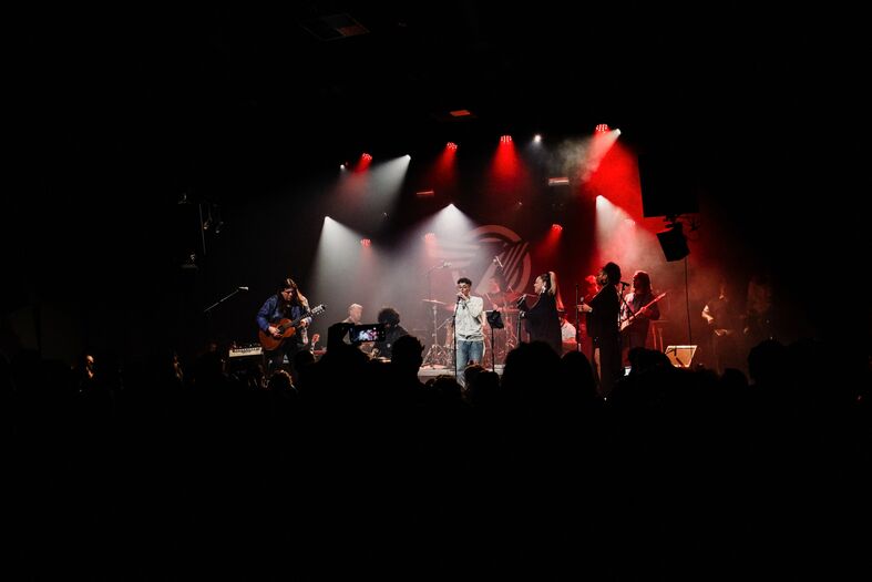 Een live muziekoptreden op een podium met bandleden en kleurrijke verlichting in een donkere ruimte.