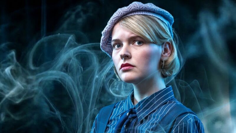 Jonge vrouw met blond haar en een baret, gekleed in een gestreepte blouse, omringd door blauwe rook.