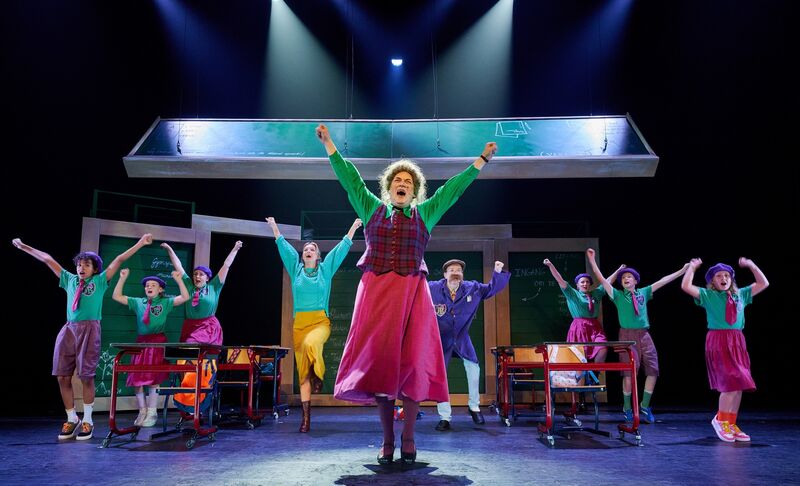 Een toneelgroep voert een musical op met kleurenrijke kostuums en enthousiaste dansers op een verlicht podium.
