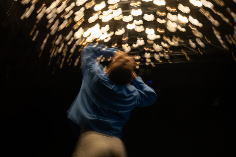 Een persoon met een blauwe shirt kijkt omhoog naar een plafond vol sprankelende lichtpunten.