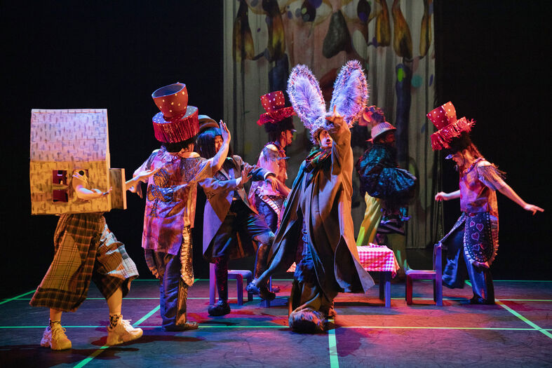 Een kleurrijke theatervoorstelling met acteurs in unieke kostuums en hoeden, die een dynamische scène opvoeren.
