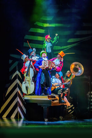 Groep muzikanten in kleurrijke kostuums spelen op een podium met een theatrale achtergrond.