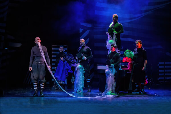 Een podium met performers in kostuums, gefocust op een zanger, met een blauwe achtergrond en theatrale belichting.