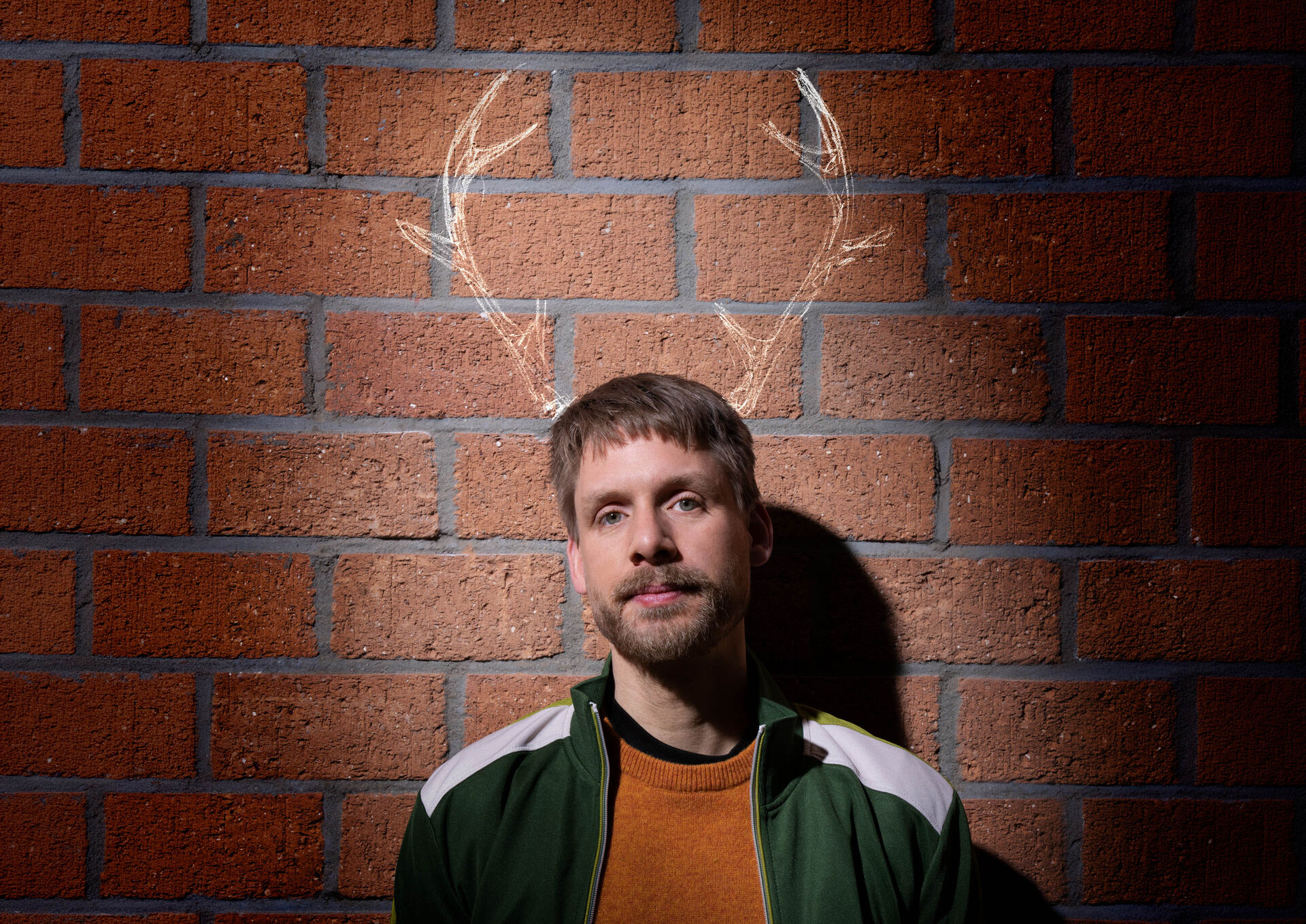 Thijs van de Meeberg staat voor een bakstenen muur met licht getekende hertengeweien boven het hoofd.