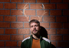 Thijs van de Meeberg staat voor een bakstenen muur met licht getekende hertengeweien boven het hoofd.