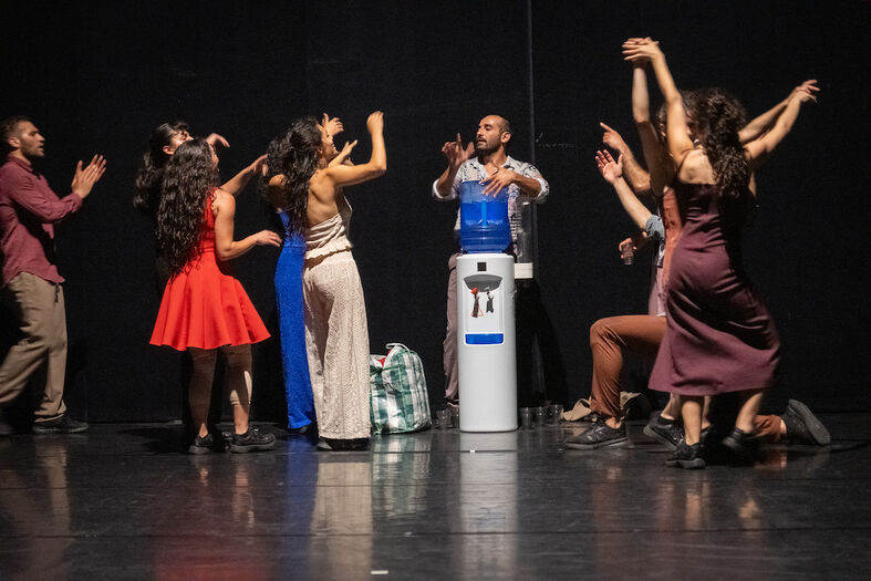 Grote groep dansers staan rond een drinkwatertank op een podium.