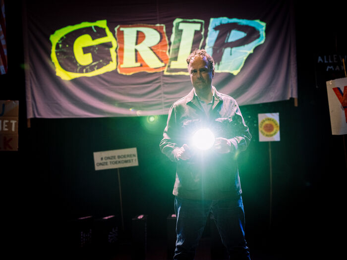 Man met een zaklamp voor een kleurrijk "GRIP" bord in een donkere setting.