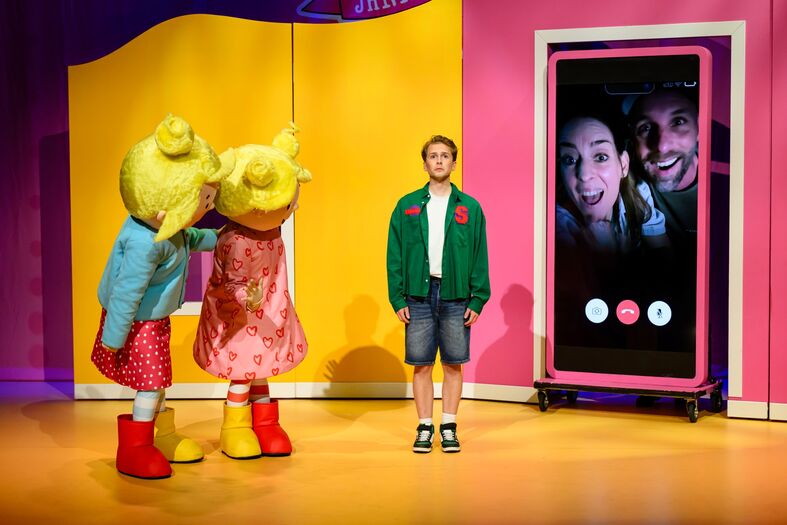 Een jongen staat tussen twee kostuumfiguren die hem ontmoeten, met een smartphone-scherm op de achtergrond.