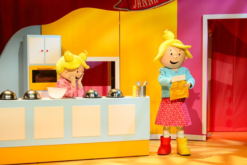Twee kleurrijke personages in een keukensetting, één leest recepten terwijl de ander bezig is met koken.