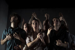 Groep mensen in een dramatische pose, met handen omhoog, tegen een donkere achtergrond. Emotie en intensiteit zijn zichtbaar.