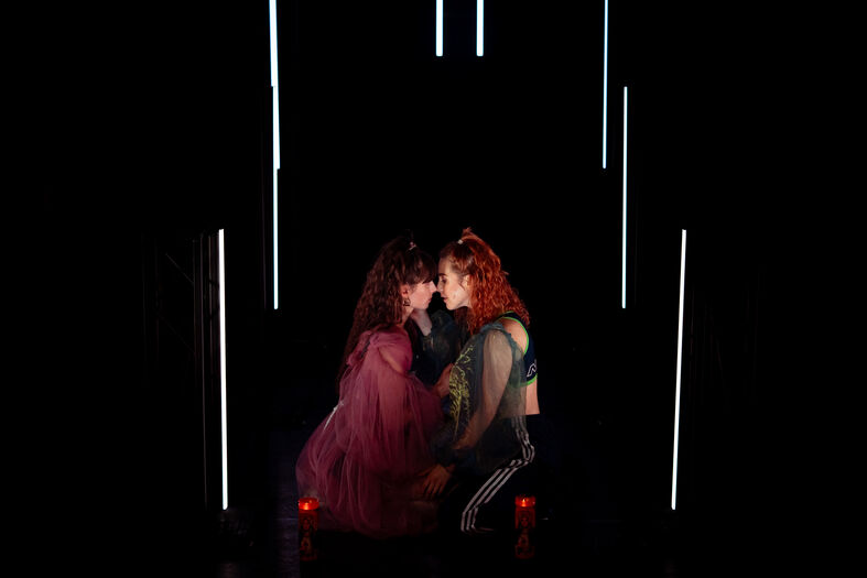 Twee performers in een donker decor met achtergrondverlichting, intiem met elkaar in interactie.