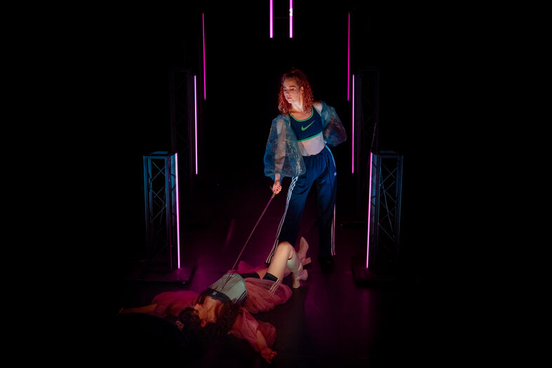 Vrouw die een persoon aan een lijn begeleidt in een donkere omgeving met neonverlichting.
