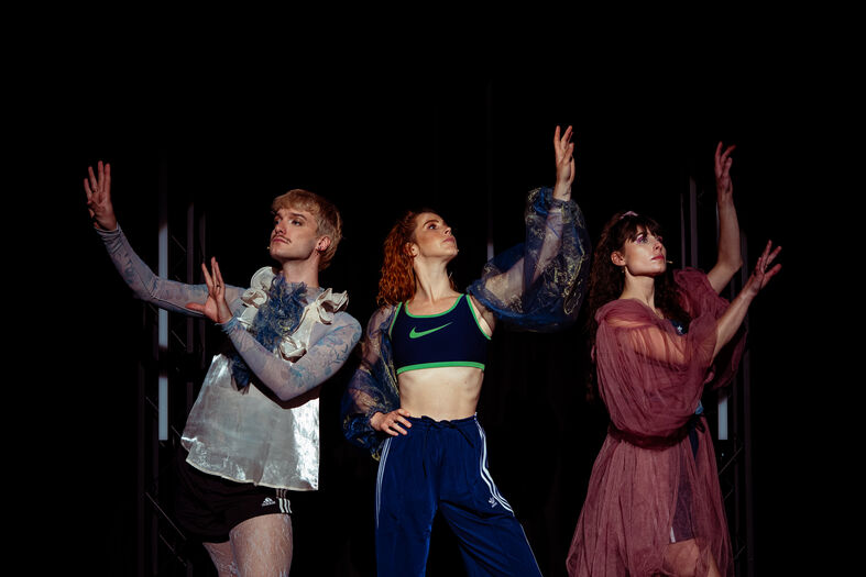 Drie danseressen in verschillende outfits poseren dramatisch op een donkere achtergrond.