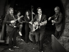 Een band bestaande uit vijf muzikanten speelt samen in een donkere setting, met verschillende instrumenten.