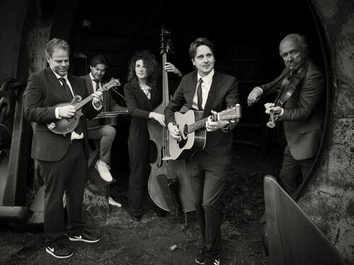 Een band bestaande uit vijf muzikanten speelt samen in een donkere setting, met verschillende instrumenten.