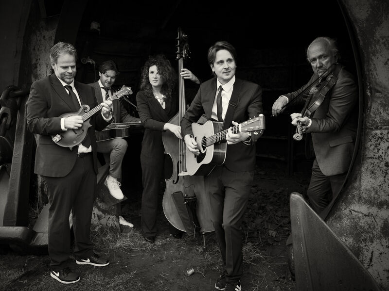 Een band bestaande uit vijf muzikanten speelt samen in een donkere setting, met verschillende instrumenten.