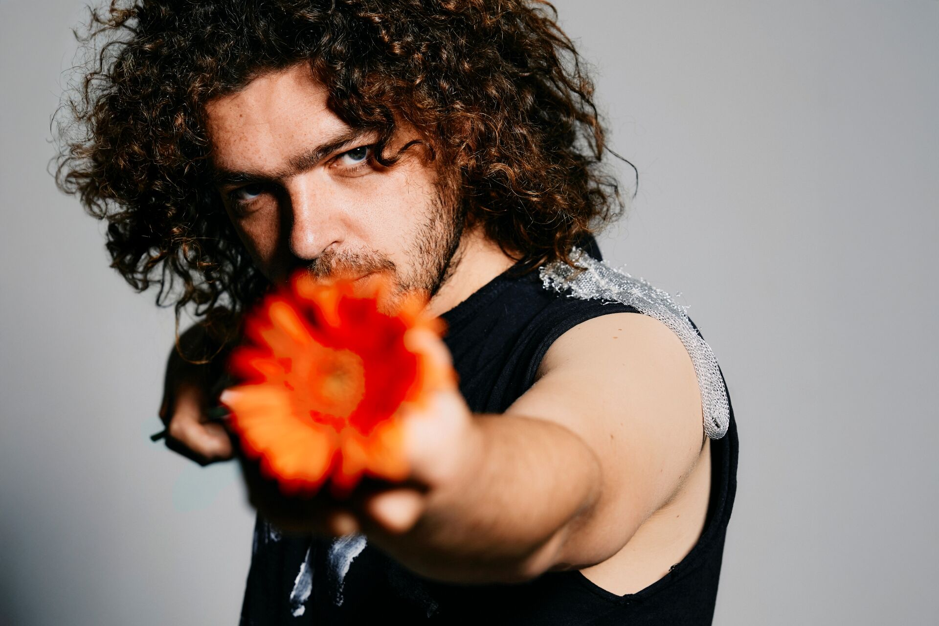 Flip Noorman met krullend haar richt een feloranje bloem scherp naar de camera.