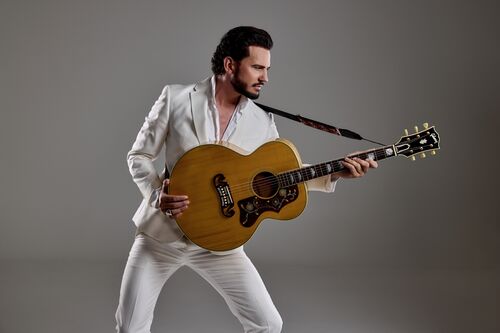 Een man in een wit pak speelt een grote, gouden gitaar met een intense blik.