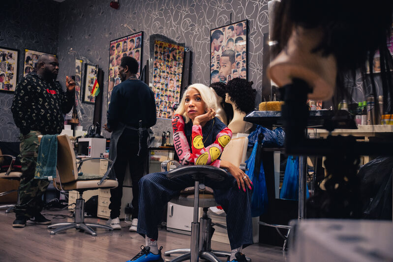 Meisje in een kapsalon, wachtend op haar beurt terwijl kappers klanten bedienen. Achtergrond met foto’s aan de muur.