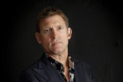 Portret foto van Huub van der Lubbe in een een pak met blouse met motief.