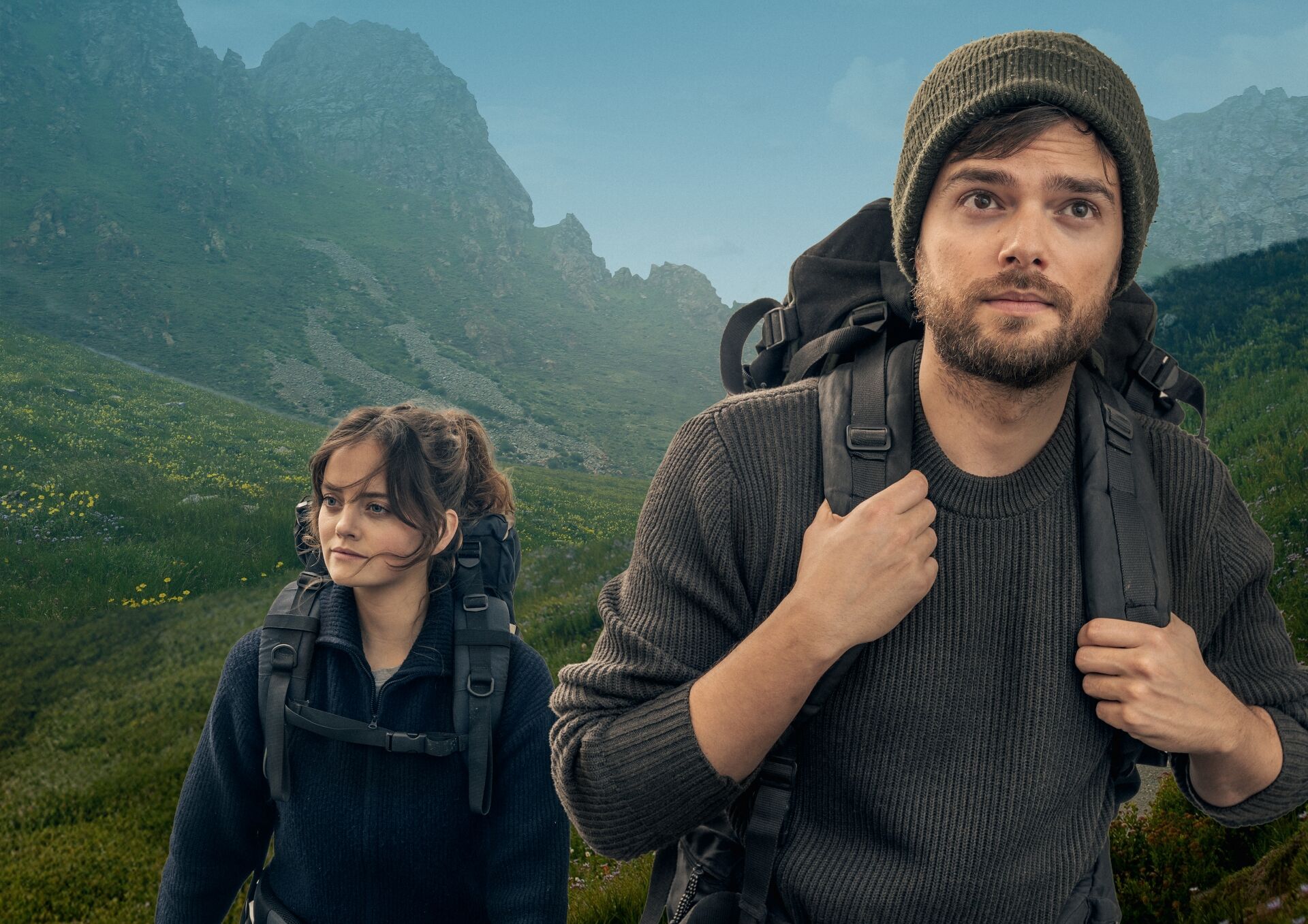 Twee wandelaars in een bergachtig landschap, kijkend naar de horizon met backpacks op hun rug.