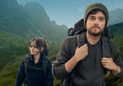 Twee wandelaars in een bergachtig landschap, kijkend naar de horizon met backpacks op hun rug.