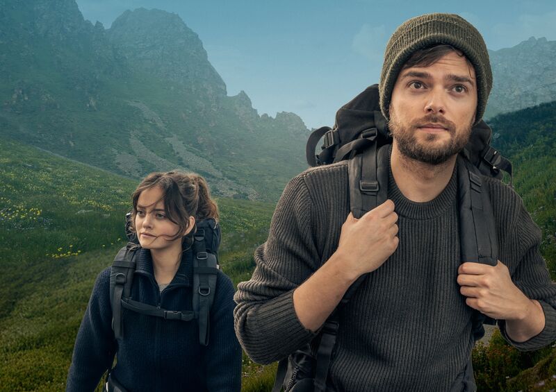 Twee wandelaars in een bergachtig landschap, kijkend naar de horizon met backpacks op hun rug.