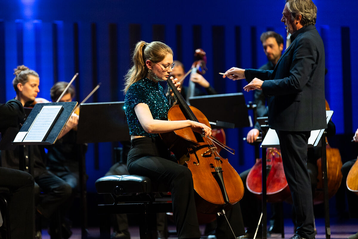 Een celliste speelt in een orkest tijdens een live optreden, onder toezicht van de dirigent.