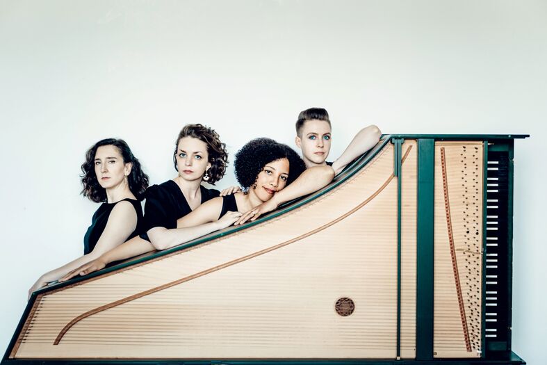 Vijf vrouwen leunend op een klavecimbel, pose voor een muzikale fotoshoot.