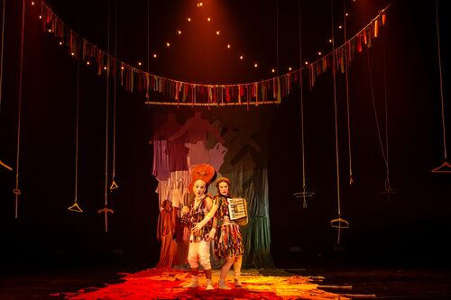 Twee performers in kleurrijke kostuums op een podium met sfeervolle verlichting en decoratieve vlaggetjes.