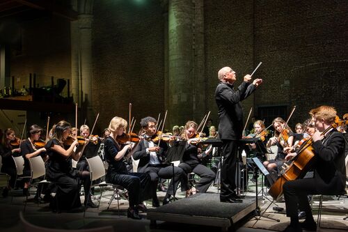 Een dirigent leidt een orkest van muzikanten in een sfeervolle concertzaal.
