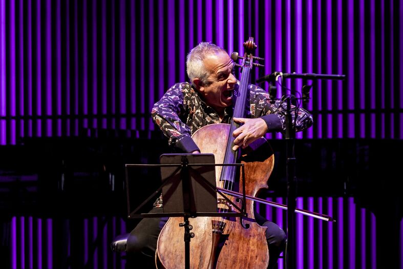Een cellist speelt op een podium met paarse verlichting, met een muziekstandaard voor zich.