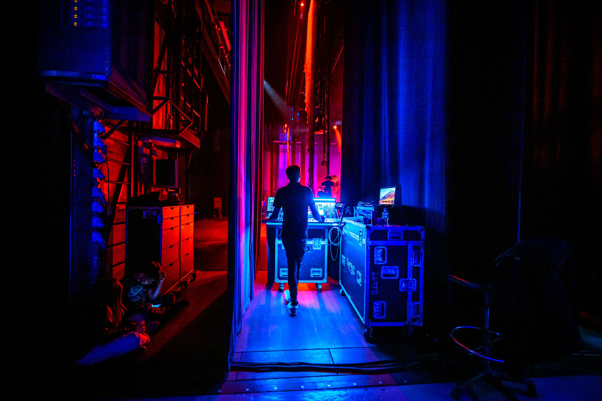 Een persoon loopt achter het podium, verlicht door achtergrondverlichting in blauwe en rode tinten.