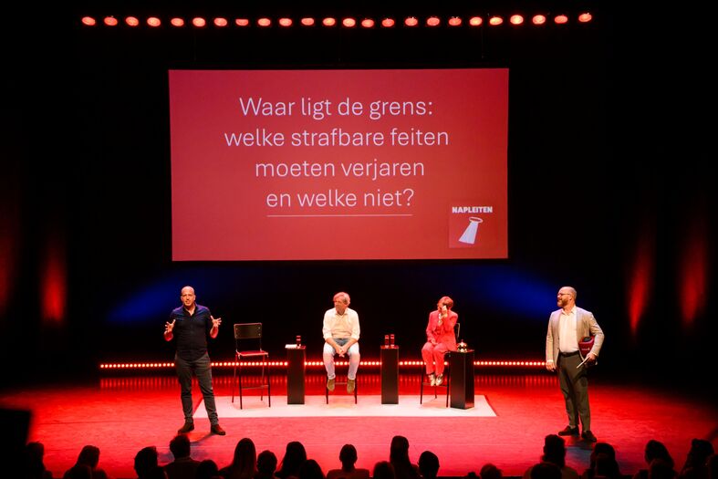 Een podium met sprekers en een groot scherm met de tekst: "Waar ligt de grens; welke vreemde feiten moeten veranderen en welke niet?"