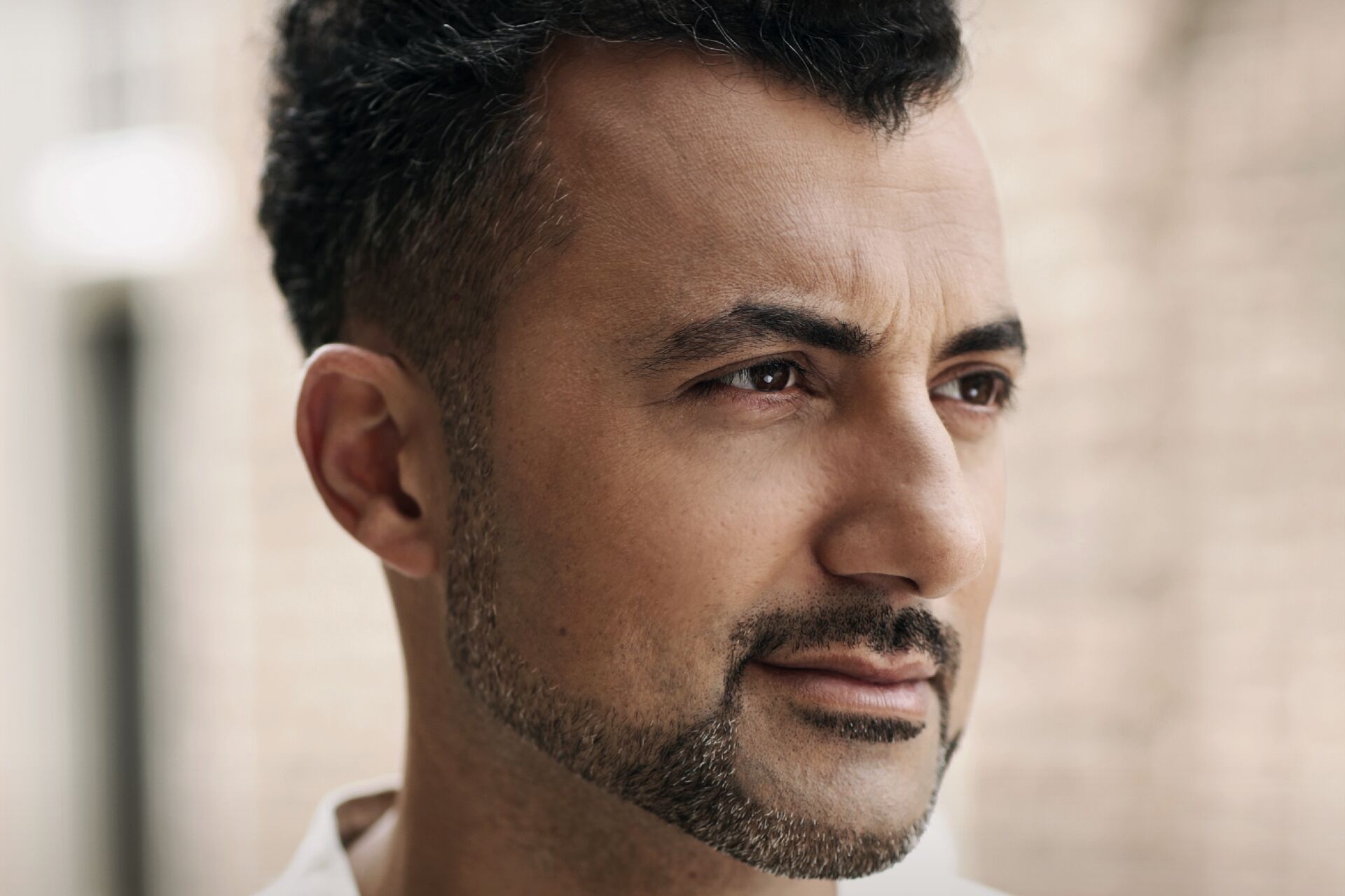 Portret van een man met een korte baard, kijkend naar de rechterzijde, met een neutrale achtergrond.