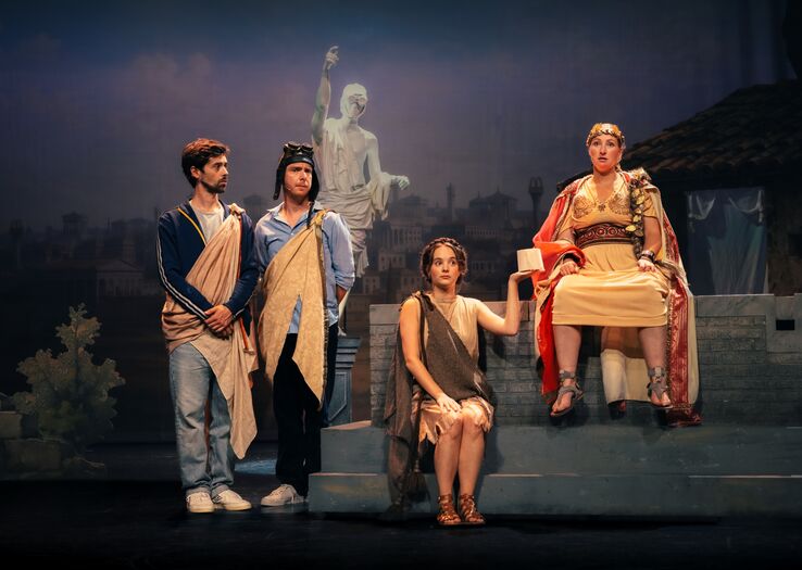 Theaterafbeelding van vier acteurs in antieke kostuums, zittend of staand op een podium, met een historische achtergrond.