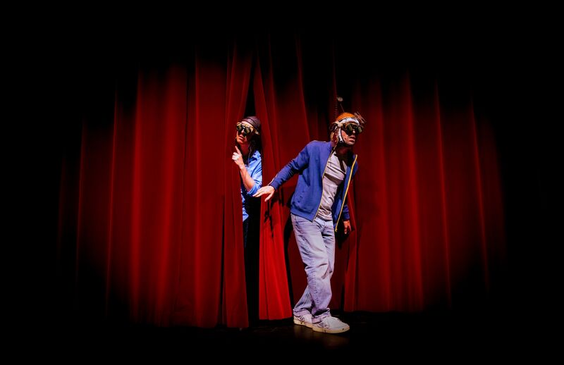 Twee kinderen komen het podium op, terwijl ze een rode theatergordijn openschuiven.