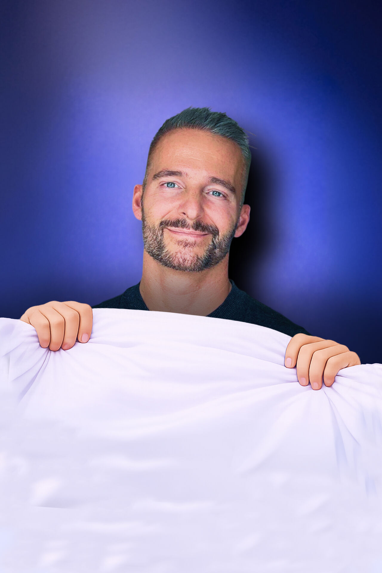 Een man met een lichte baard houdt een witte doek vast en kijkt glimlachend naar de camera.