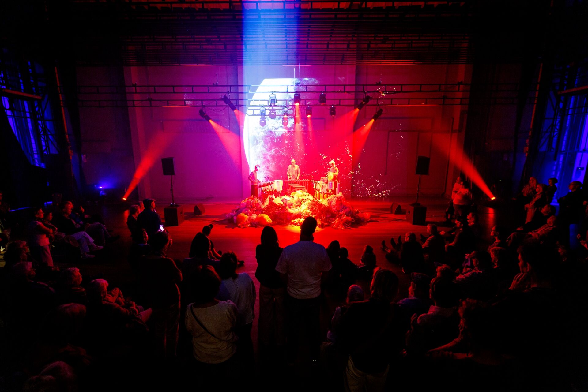 Een levendige concertomgeving met een podium, muzikanten en een publiek onder kleurrijke verlichting.